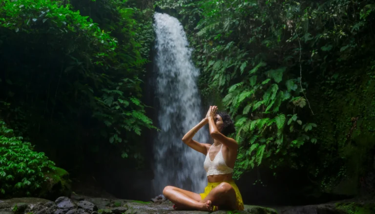 Ragazza in mezzo alla foresta che medita vicino ad una cascata