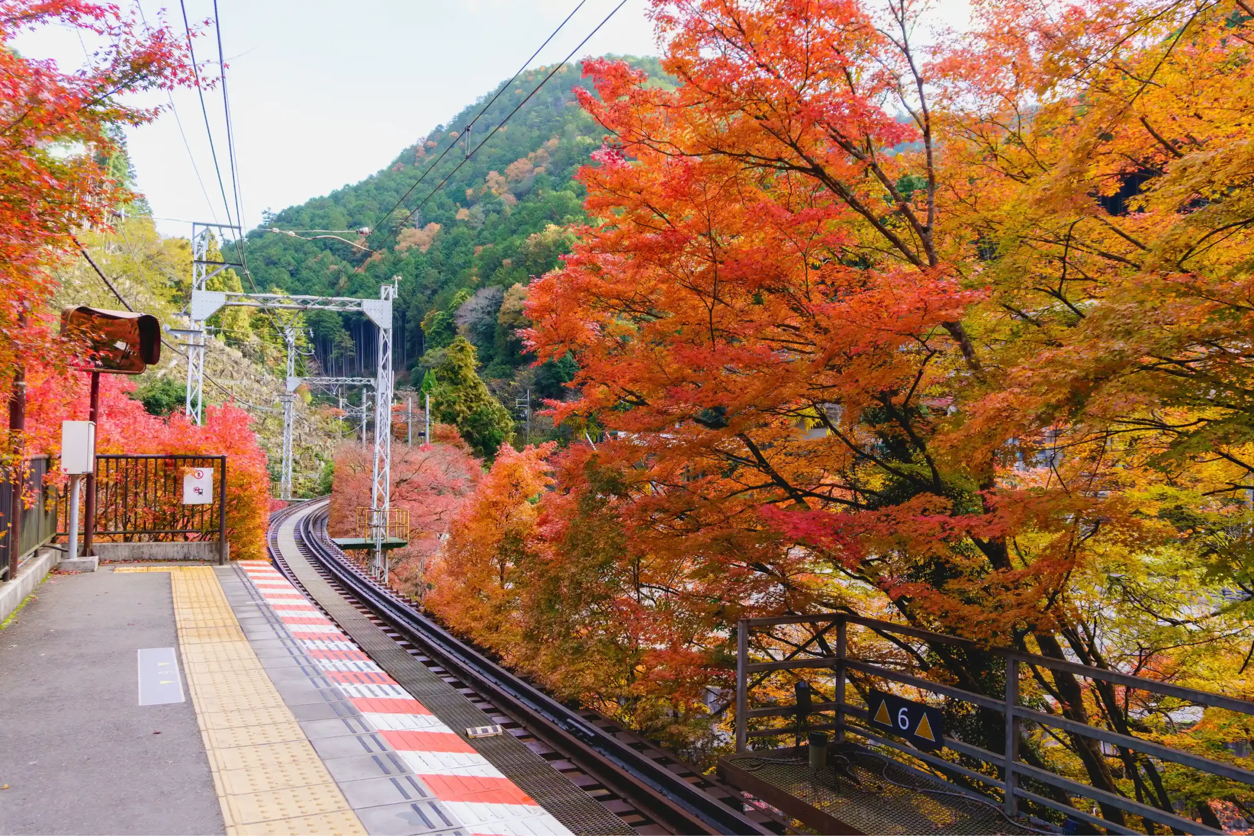 Fermata del treno giapponese circondata da alberi dai colori autunnali e montagne